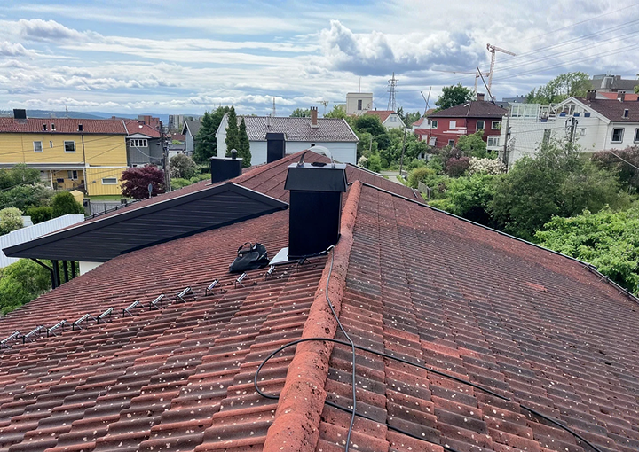 Tradisjonelt skråtak med tegltakstein, sentralt plassert svart pipe og mønestein lagt i opphøyd mørtelfuge.