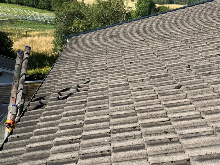 Værslitt, grått tak med overlappende betong- eller takstein og en stige lent mot kanten.