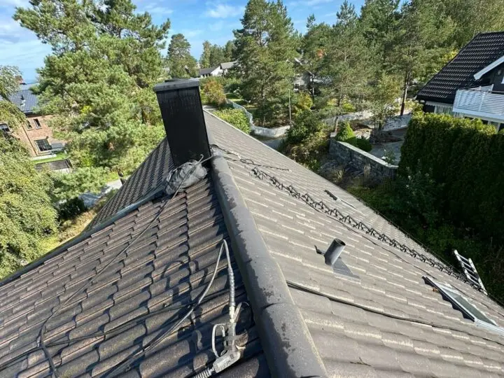 Utstyr for takrens eller overflatebehandling med en sprøytestav plassert på mørke betongtakstein.