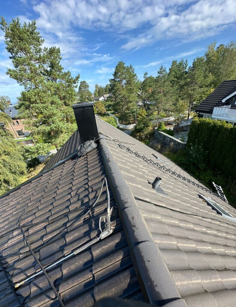 Utstyr for takrens eller overflatebehandling med en sprøytestav plassert på mørke betongtakstein.