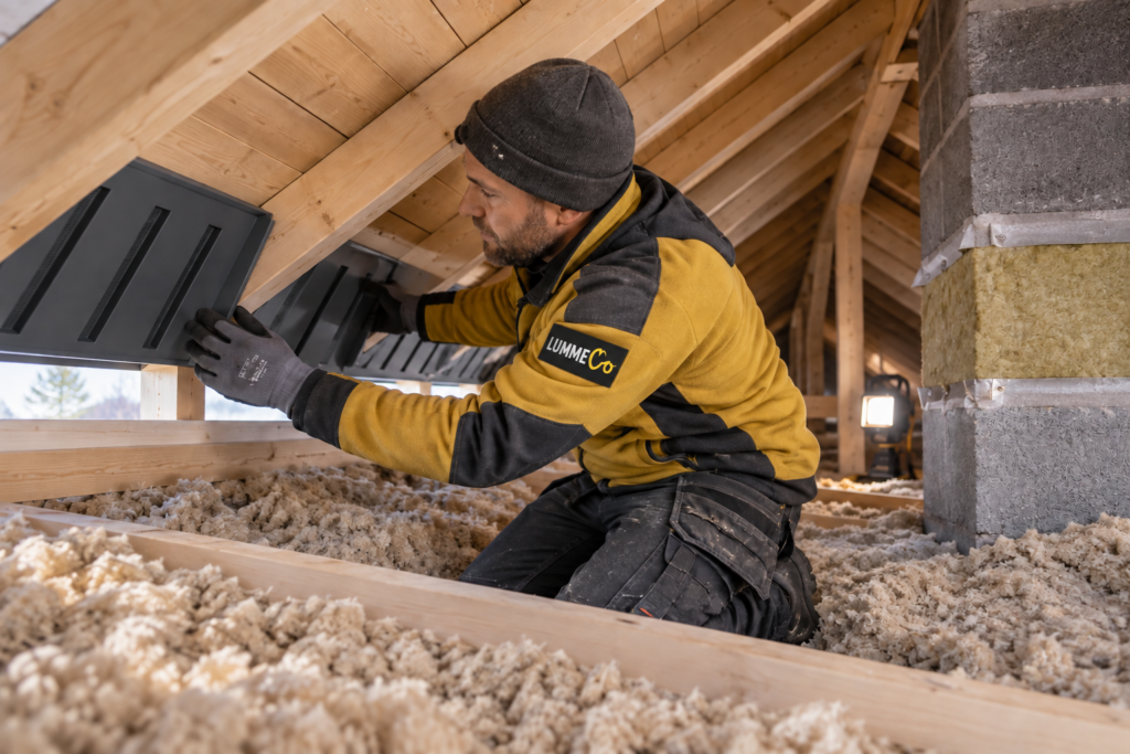 Arbeider som monterer isolasjon og ventilasjonsplater i et uferdig loftsrom.