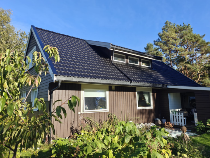 Toetasjes bolig med brunt stående trekledning, mørkt skråtak med takstein og et lite kvistvindu.