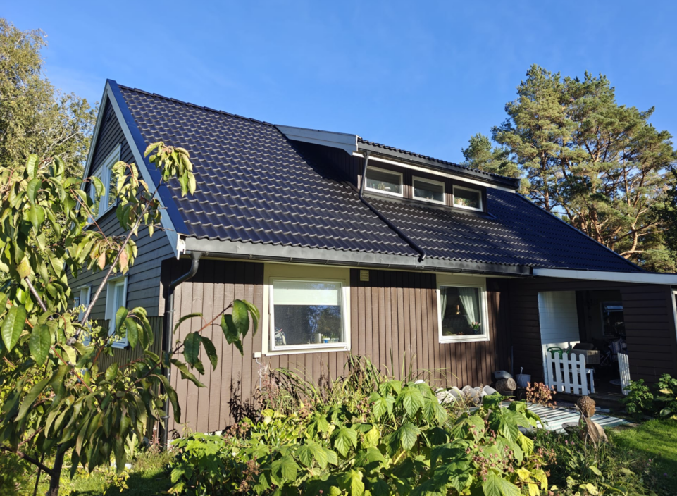 Toetasjes bolig med brunt stående trekledning, mørkt skråtak med takstein og et lite kvistvindu.